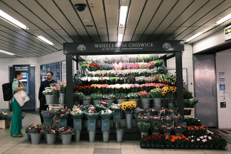 A flower display at Wheeler of Chiswick inside an underground station, showcasing an arrangement of fresh flowers including pink, white, yellow, and red blooms such as roses, daisies, and tulips, orga