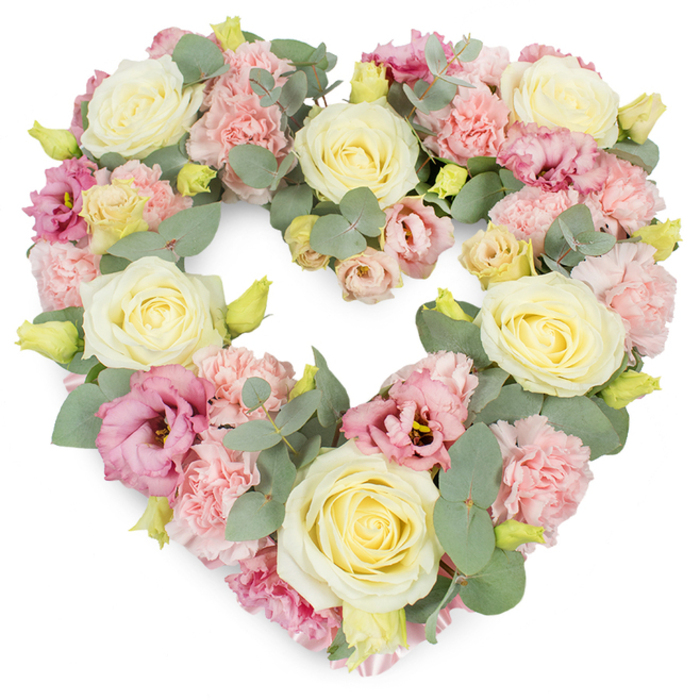 A meticulously crafted heart-shaped funeral wreath is shown in full against a bright white background, its shape clear and symmetrical, like a carefully drawn love token. The heart is densely covered with flowers, dominated by creamy ivory and pale lemon roses that serve as the main anchors of the design. Each rose is beautifully formed, with layered petals spiralling from a tight centre to softly cupped outer edges, giving a sense of classic elegance and steady devotion. Between these focal roses, clusters of pastel pink carnations fill the spaces, their frilled petals overlapping to create a plush, almost fabric-like texture that softens the entire wreath. Scattered among them, deeper pink to mauve lisianthus blooms open in loose, fluted forms, lending a slightly more contemporary note and subtle shifts in tone, much like the gentle changes of light over the fields on the edge of Chelmsford. Thin stems of eucalyptus are woven throughout the arrangement, their round, silvery-green leaves peeking out from between the blossoms, adding depth, freshness, and a hint of woodland coolness. Here and there, tiny yellow-green buds lift the design, suggesting resilience and hope even in sorrow. Every bloom is placed with care, ensuring the heart outline is clear and complete, a visual embrace for the person being honoured. This kind of tribute feels fitting for a funeral or memorial service in Chelmsford, perhaps at a church near Springfield or a chapel at Chelmsford Crematorium, where families gather to share memories. The overall impression is one of tenderness, calm, and deep respect, with the pastel colours and soft textures offering comfort during difficult goodbyes.