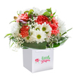 There is a sense of effortless joy and natural elegance that radiates from this Chelmsford-crafted bouquet, artfully arranged within a spotless white gift bag. Soft coral and vibrant red carnations beckon with their plush, frilled petals, creating a gentle yet dynamic interplay of warmth and colour reminiscent of spring mornings by Oaklands Park. Crisp white daisies with their eye-catching golden-green centers bring a note of playful happiness, while wispy baby's breath floats throughout, its tiny blossoms evoking a sense of gentle innocence and fleeting beauty. Two or three closed, purple-hued buds nestled to one side hint at new beginnings, adding depth and a subtle pop of colour amid the lushness. Broad, polished green leaves wrap around the base, anchoring the arrangement and reflecting the robust greenery found in Chelmsford's gardens. The light falls evenly, emphasizing the bouquet's freshness and the skill of the local florist who has placed every stem with obvious care. Prepared in a sturdy, ribbon-handled gift bag that signals both ready gifting and local delivery, this arrangement promises to brighten occasions from birthdays in Springfield to friendly pick-me-ups on Broomfield Road. Every detail speaks of celebration, sincerity, and the simple pleasure of sharing Chelmsford's floral beauty with someone you cherish.